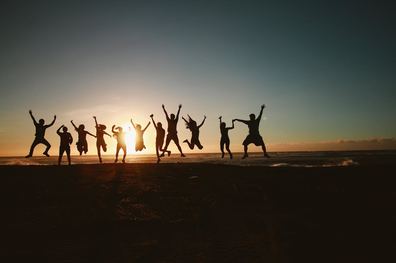 About Silhouette of a group of friends jumping on a beach at sunset, expressing joy and freedom.